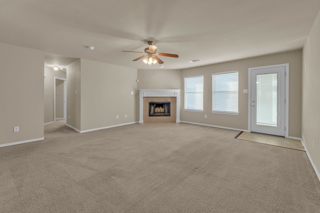 unfurnished living room with light carpet, ceiling fan, and a tiled fireplace