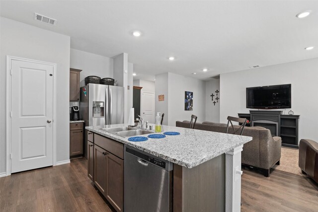 kitchen featuring light stone countertops, sink, dark wood-type flooring, stainless steel appliances, and a center island with sink