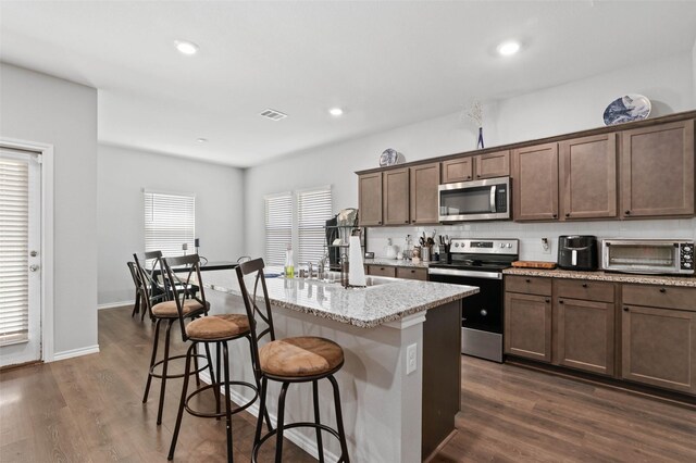 kitchen featuring a kitchen bar, light stone counters, stainless steel appliances, a center island with sink, and dark hardwood / wood-style floors