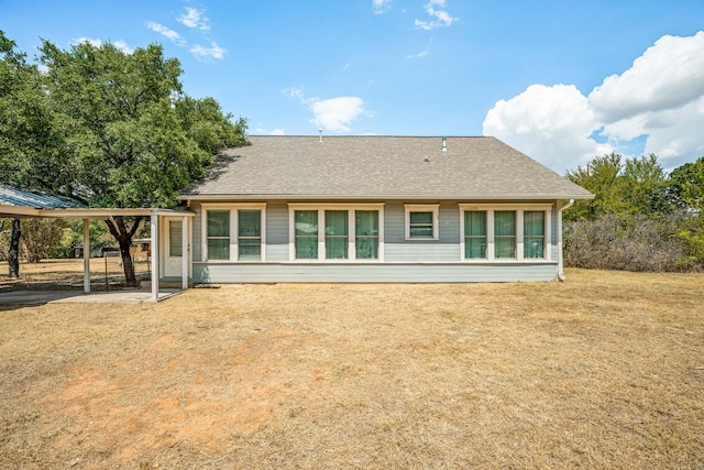 rear view of house with a shingled roof and a lawn