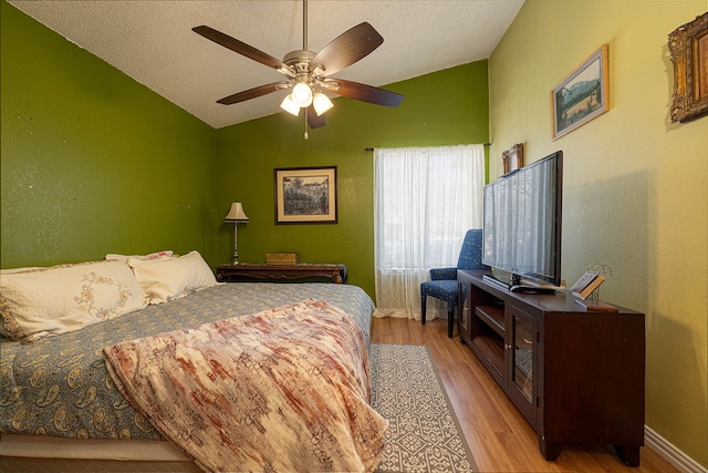 bedroom featuring ceiling fan, lofted ceiling, a textured ceiling, and light hardwood / wood-style flooring