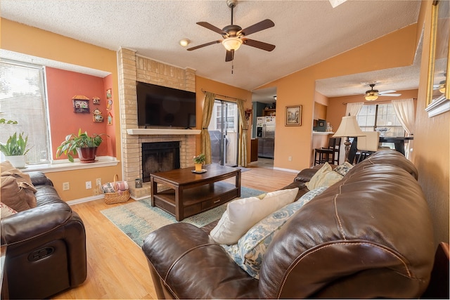 living room with vaulted ceiling, hardwood / wood-style flooring, ceiling fan, a fireplace, and a textured ceiling