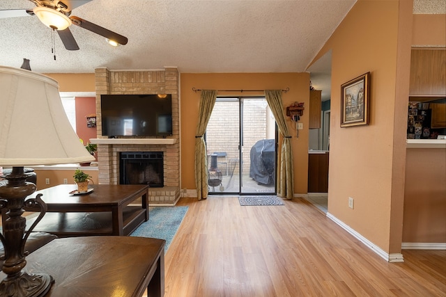 living room with a fireplace, ceiling fan, light hardwood / wood-style flooring, and a textured ceiling