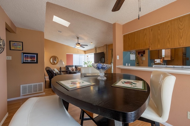 dining space with a textured ceiling, light hardwood / wood-style floors, lofted ceiling with skylight, and ceiling fan