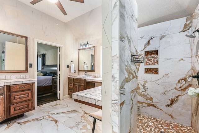 bathroom with vanity, ceiling fan, a textured ceiling, and tiled shower