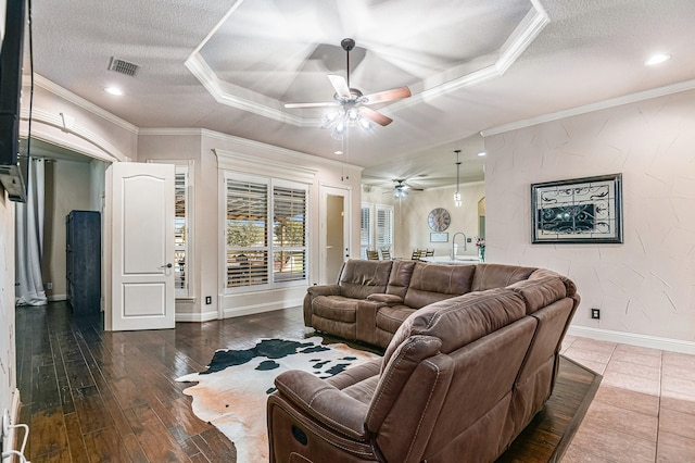 living room with ceiling fan, a tray ceiling, ornamental molding, and a textured ceiling