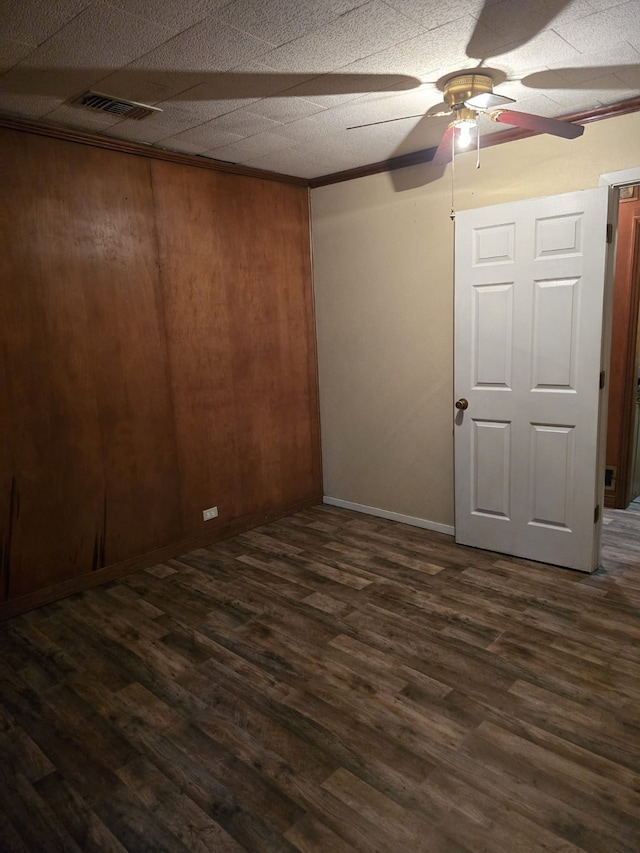 unfurnished room with dark wood-type flooring, ceiling fan, and wood walls