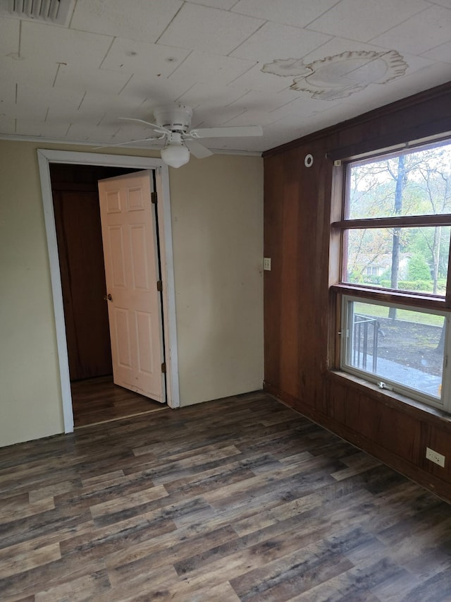 spare room featuring dark wood-type flooring, wooden walls, and ceiling fan