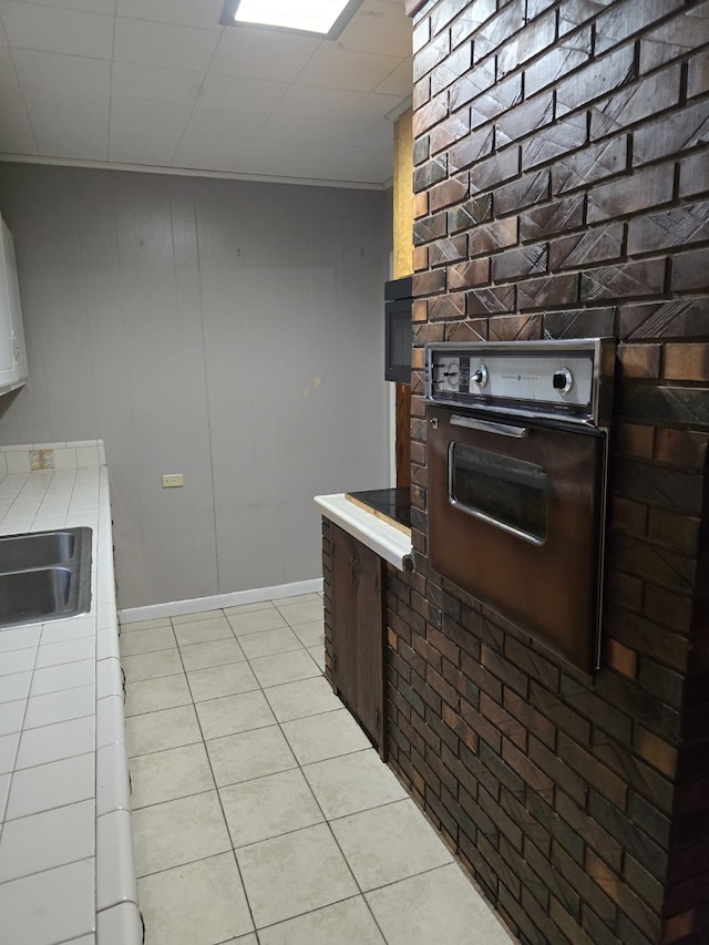 708 Walnut St, Atlanta, TX 75551 - kitchen featuring tile counters, wall oven, a sink, light tile patterned floors, and baseboards