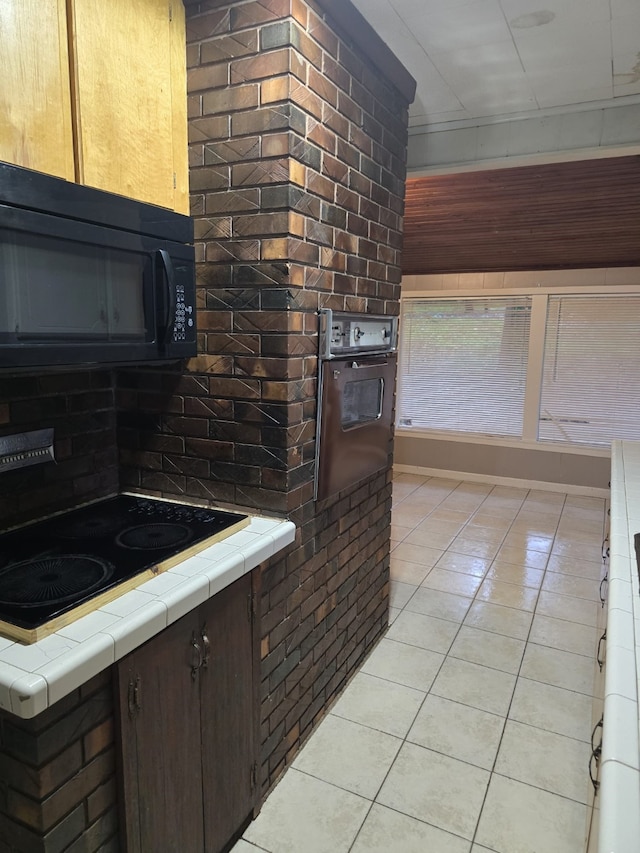 kitchen with tasteful backsplash, tile counters, light tile patterned floors, dark brown cabinetry, and black appliances