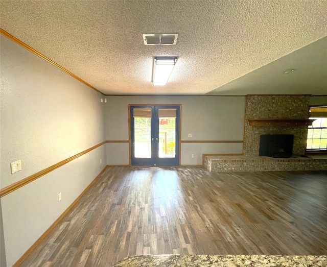 unfurnished living room featuring french doors, ornamental molding, a textured ceiling, a fireplace, and dark hardwood / wood-style floors