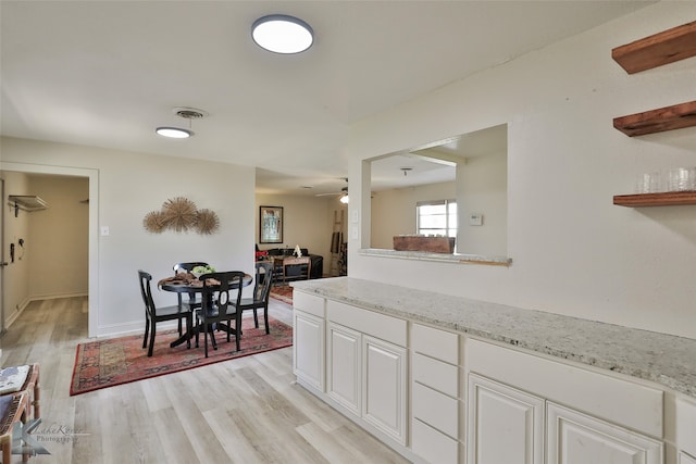 kitchen with ceiling fan, white cabinets, light stone countertops, and light wood-type flooring