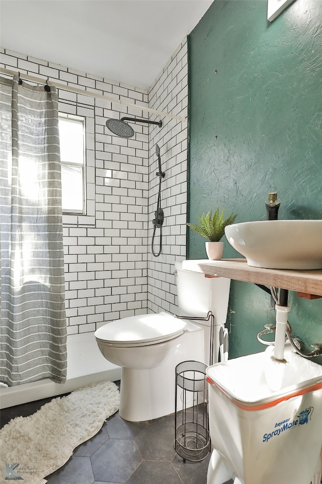 bathroom with toilet, tile patterned flooring, and tiled shower