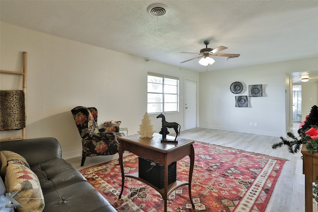 living room with a textured ceiling, light wood-type flooring, and ceiling fan