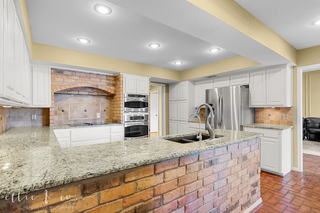 kitchen with sink, appliances with stainless steel finishes, white cabinetry, backsplash, and light stone countertops