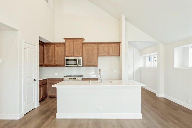 kitchen featuring tasteful backsplash, an island with sink, sink, stove, and light hardwood / wood-style floors