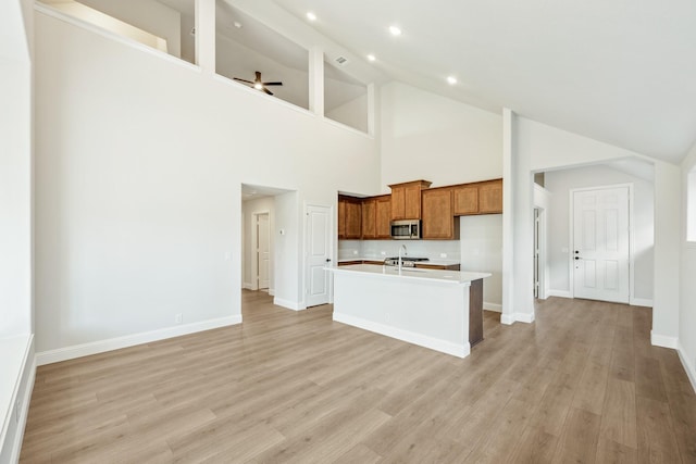 kitchen with high vaulted ceiling, light hardwood / wood-style flooring, ceiling fan, and an island with sink