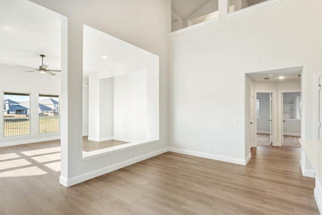 unfurnished room with a towering ceiling, light wood-type flooring, and ceiling fan