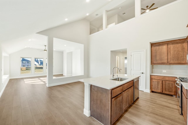 kitchen featuring a kitchen island with sink, sink, decorative backsplash, light wood-type flooring, and stainless steel appliances