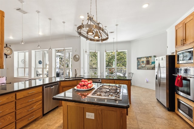 kitchen featuring appliances with stainless steel finishes, dark stone counters, sink, decorative light fixtures, and a kitchen island