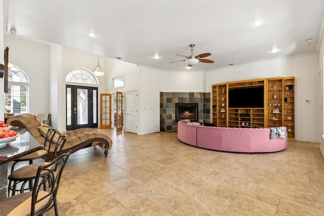 living room with french doors, ceiling fan, ornamental molding, and a tiled fireplace