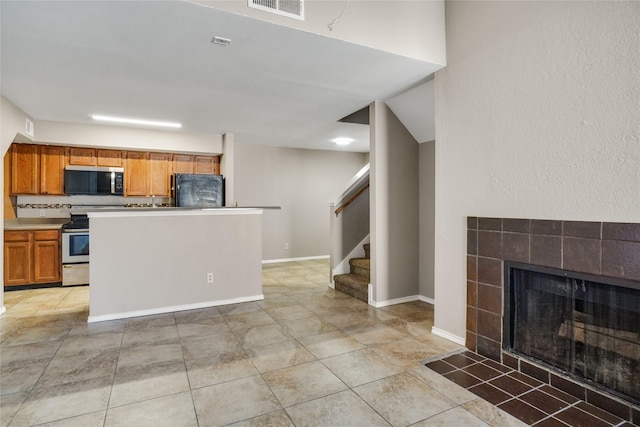 kitchen featuring a tile fireplace, stainless steel appliances, visible vents, light countertops, and brown cabinetry