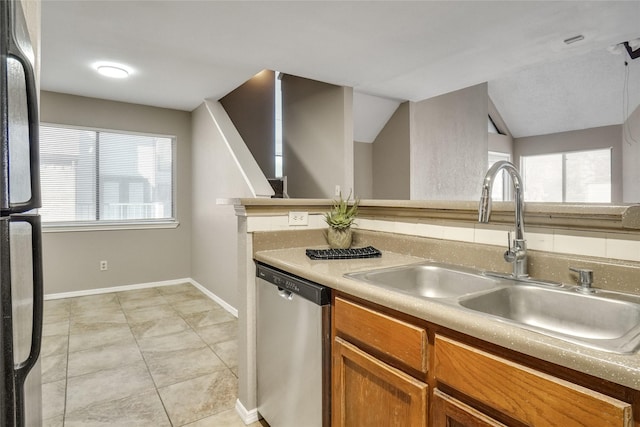 kitchen featuring brown cabinets, a sink, black refrigerator, plenty of natural light, and dishwasher