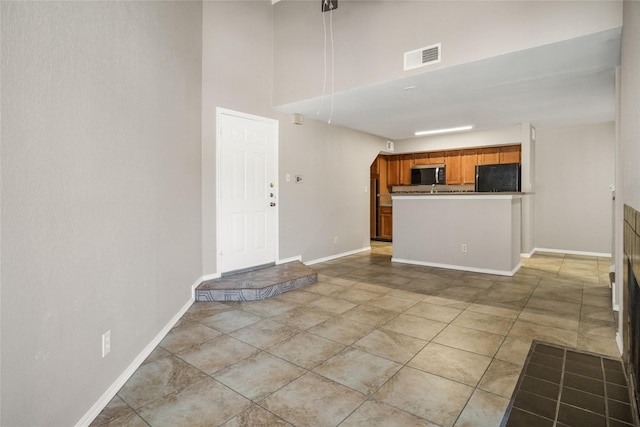 interior space featuring refrigerator, visible vents, baseboards, open floor plan, and brown cabinets