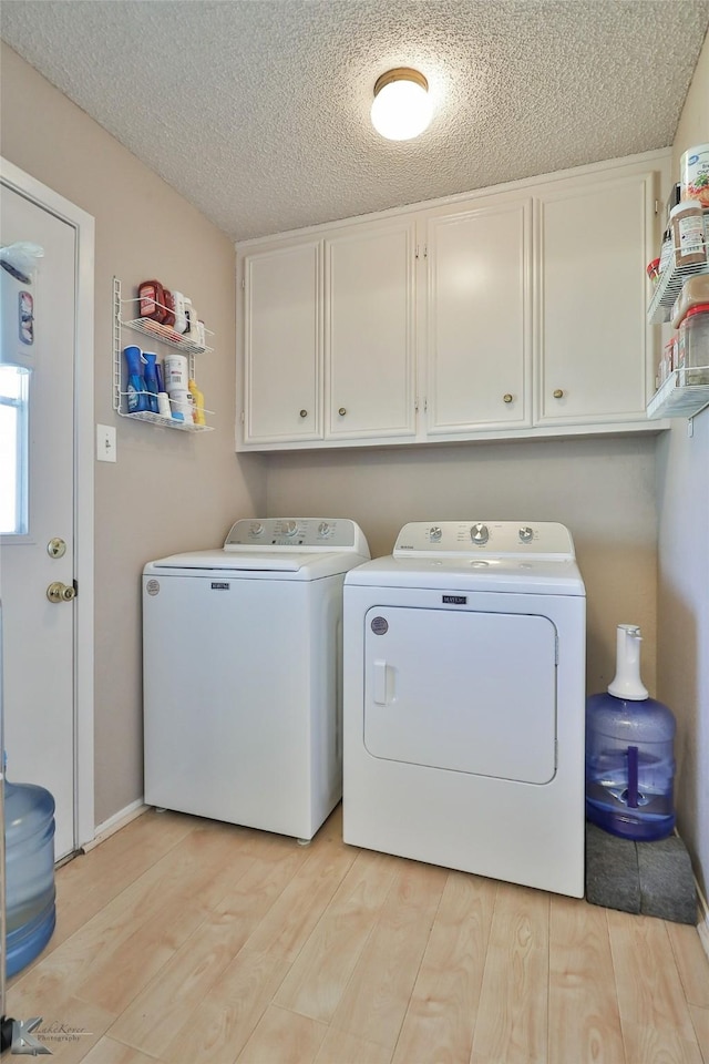 washroom with washer and clothes dryer, light hardwood / wood-style floors, cabinets, and a textured ceiling