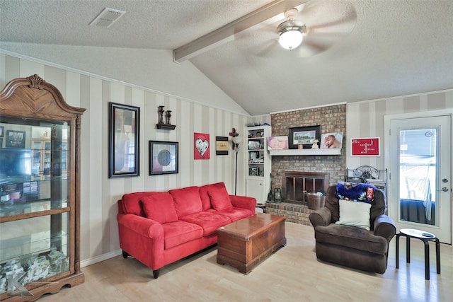 living room featuring ceiling fan, vaulted ceiling with beams, wood-type flooring, a textured ceiling, and a brick fireplace