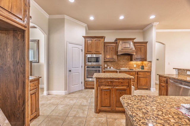 kitchen featuring light stone counters, crown molding, a kitchen island, custom range hood, and appliances with stainless steel finishes