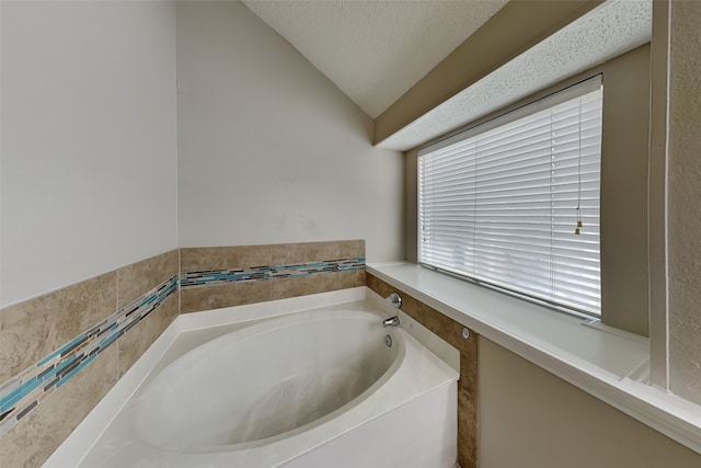 bathroom featuring a textured ceiling, a tub, and lofted ceiling