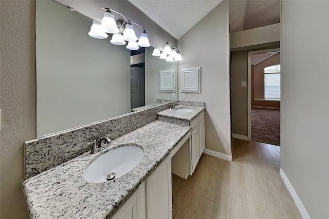 bathroom with vanity, wood-type flooring, a textured ceiling, and vaulted ceiling