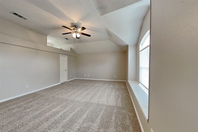 empty room with a textured ceiling, ceiling fan, carpet floors, and vaulted ceiling