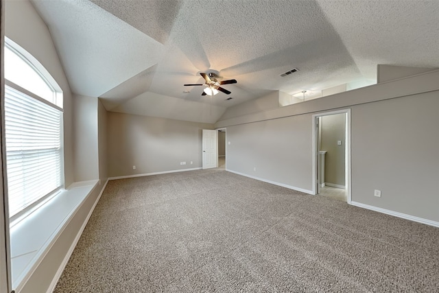 carpeted spare room with a textured ceiling, vaulted ceiling, and ceiling fan