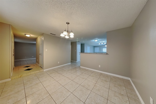 tiled empty room with a textured ceiling and a notable chandelier