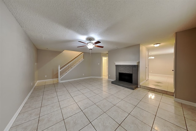 unfurnished living room featuring ceiling fan, light tile patterned floors, a textured ceiling, and a brick fireplace