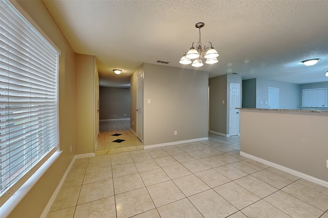 spare room featuring a textured ceiling, an inviting chandelier, and light tile patterned flooring