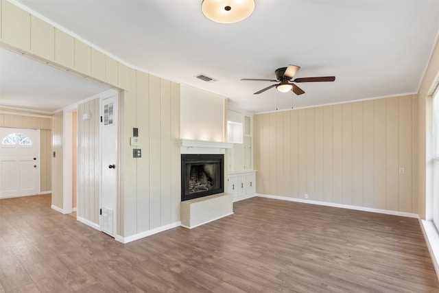 unfurnished living room with a fireplace, hardwood / wood-style flooring, ceiling fan, and wood walls