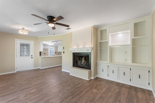 unfurnished living room with ceiling fan, dark hardwood / wood-style flooring, built in features, and a brick fireplace