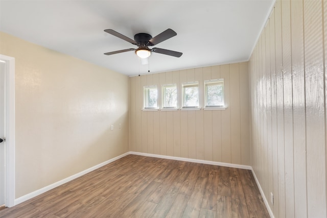 unfurnished room featuring wood-type flooring, ceiling fan, and wooden walls