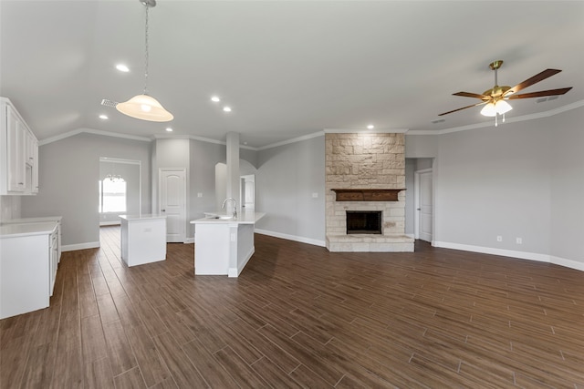 unfurnished living room with a stone fireplace, dark hardwood / wood-style floors, sink, ceiling fan, and crown molding