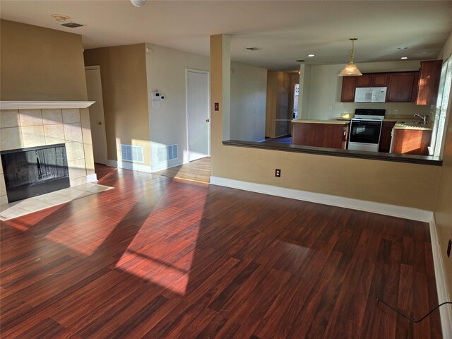 kitchen with sink, hardwood / wood-style floors, decorative light fixtures, white appliances, and a tiled fireplace