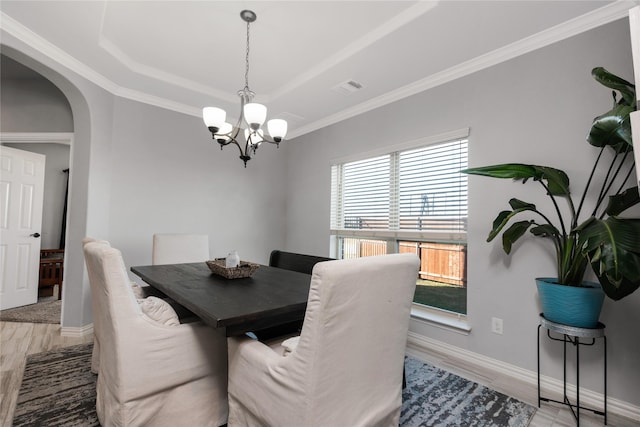 dining space with wood-type flooring, a tray ceiling, an inviting chandelier, and crown molding