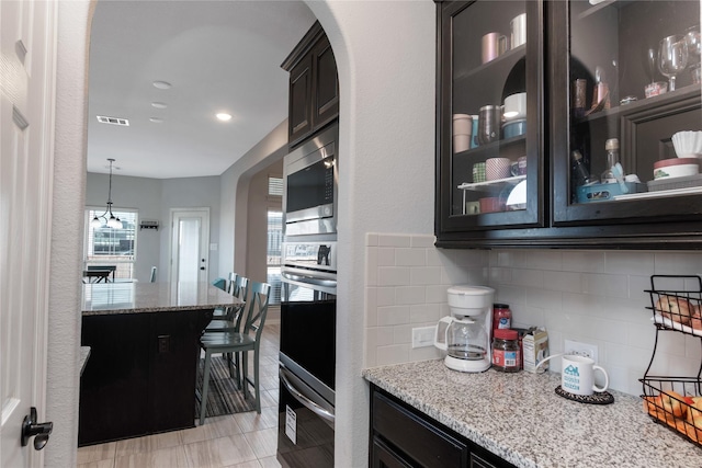 kitchen featuring pendant lighting, light stone counters, stainless steel appliances, and tasteful backsplash