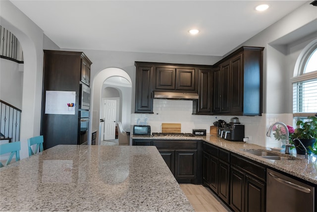 kitchen with decorative backsplash, light stone counters, dark brown cabinets, stainless steel appliances, and sink