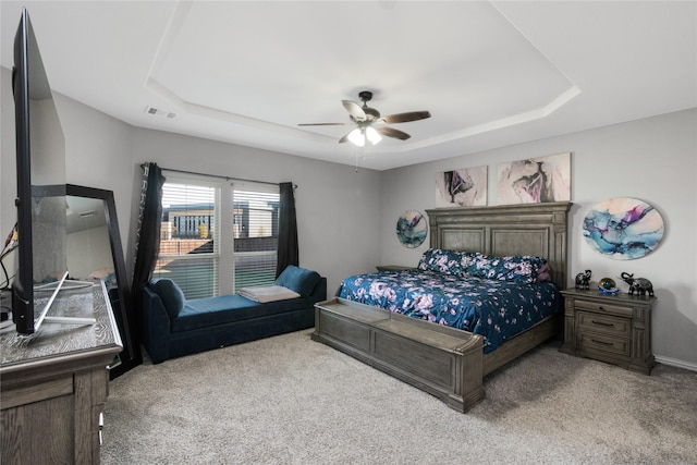 bedroom with light colored carpet, a raised ceiling, and ceiling fan