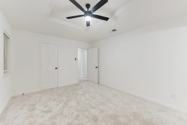 unfurnished bedroom featuring ceiling fan, light colored carpet, and a tray ceiling