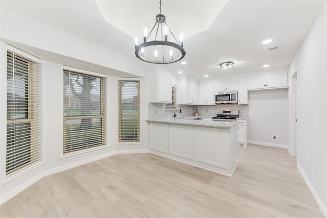 kitchen with appliances with stainless steel finishes, pendant lighting, white cabinetry, light stone counters, and kitchen peninsula