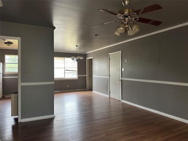 spare room featuring ornamental molding, dark wood-type flooring, ceiling fan with notable chandelier, and a healthy amount of sunlight